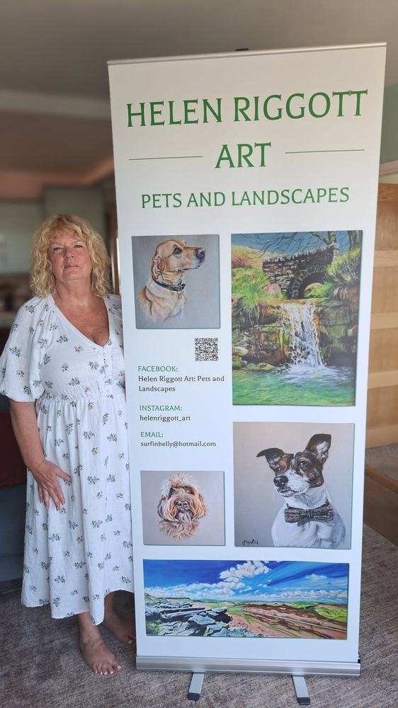 Helen Riggott standing beside her Helen Riggott Art banner